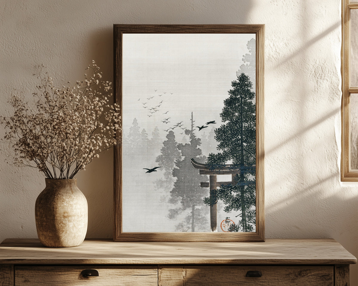 Framed art print of Flock of Birds and a Torii Gate in a Pine Forest by Ohara Koson, in a dark wood frame leaning on a rustic console beside dried flowers