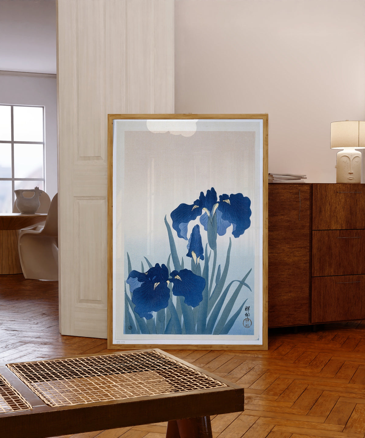 Framed art print of Irises in Blue by Ohara Koson, in a light wood frame leaning in a warm room with a parquet floor