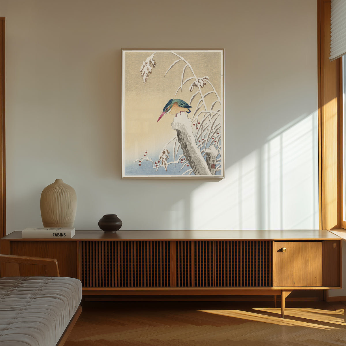 Framed art print of Kingfisher in the Snow by Ohara Koson, in a thin light frame on a sunlit wall above a wooden sideboard