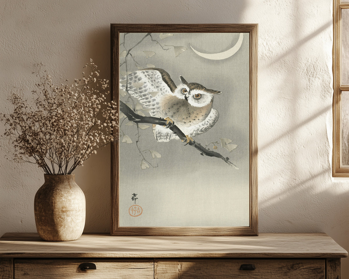 Framed art print of Long-eared Owl in Ginkgo by Ohara Koson, in a dark wood frame leaning on a rustic console beside dried flowers
