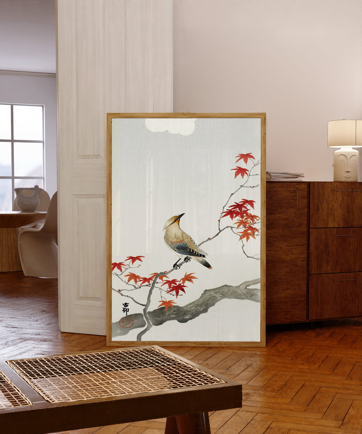 Framed art print of Waxwing on Maple by Ohara Koson, in a light wood frame leaning in a warm room with a parquet floor