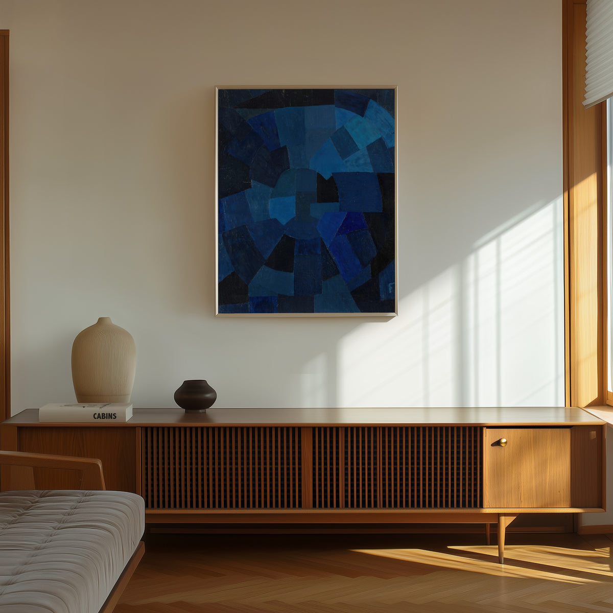 Framed art print of Komposition in Blau (1931) by Otto Freundlich, in a thin light frame on a sunlit wall above a wooden sideboard