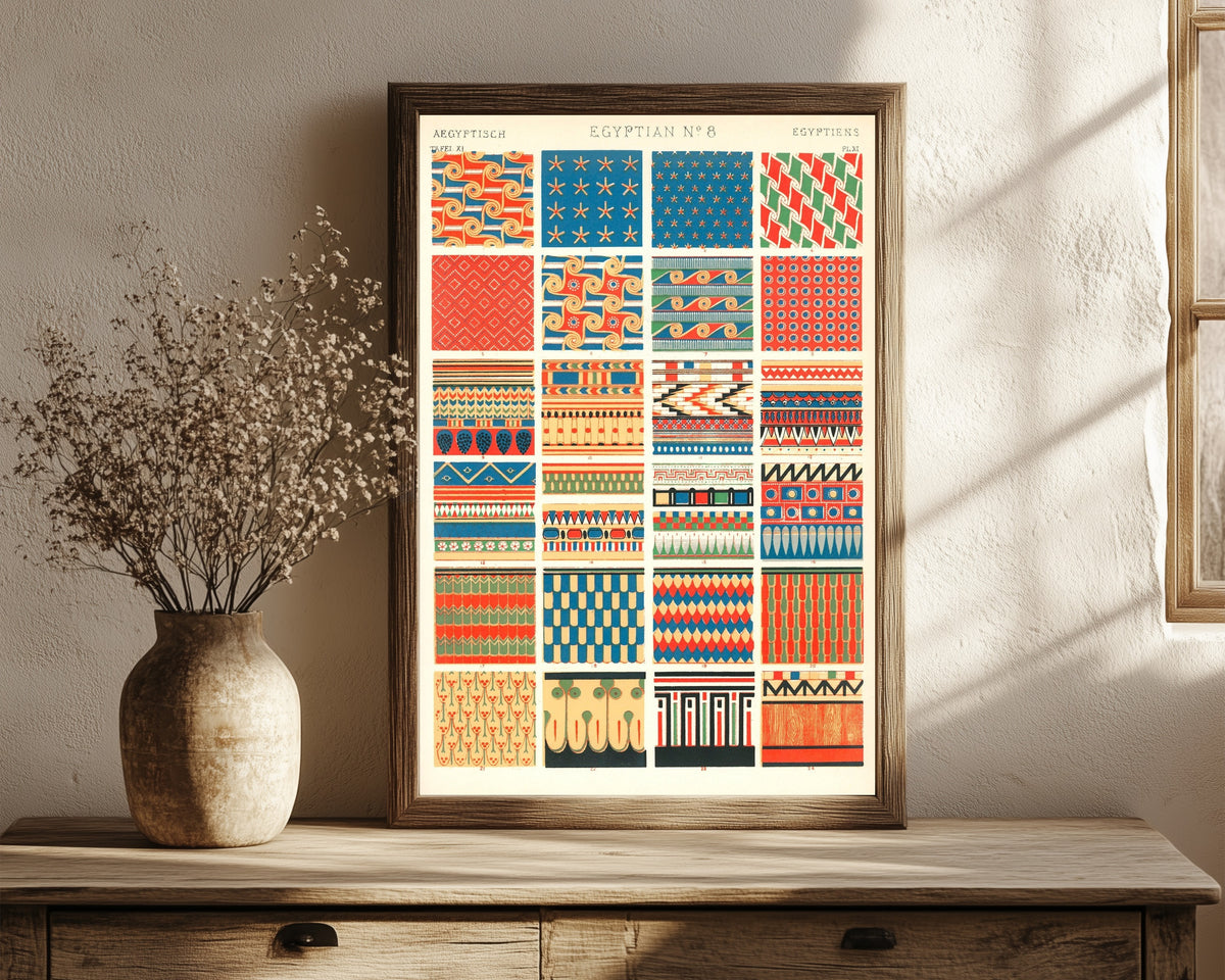 Framed art print of Egyptian by Owen Jones, in a dark wood frame leaning on a rustic console beside dried flowers