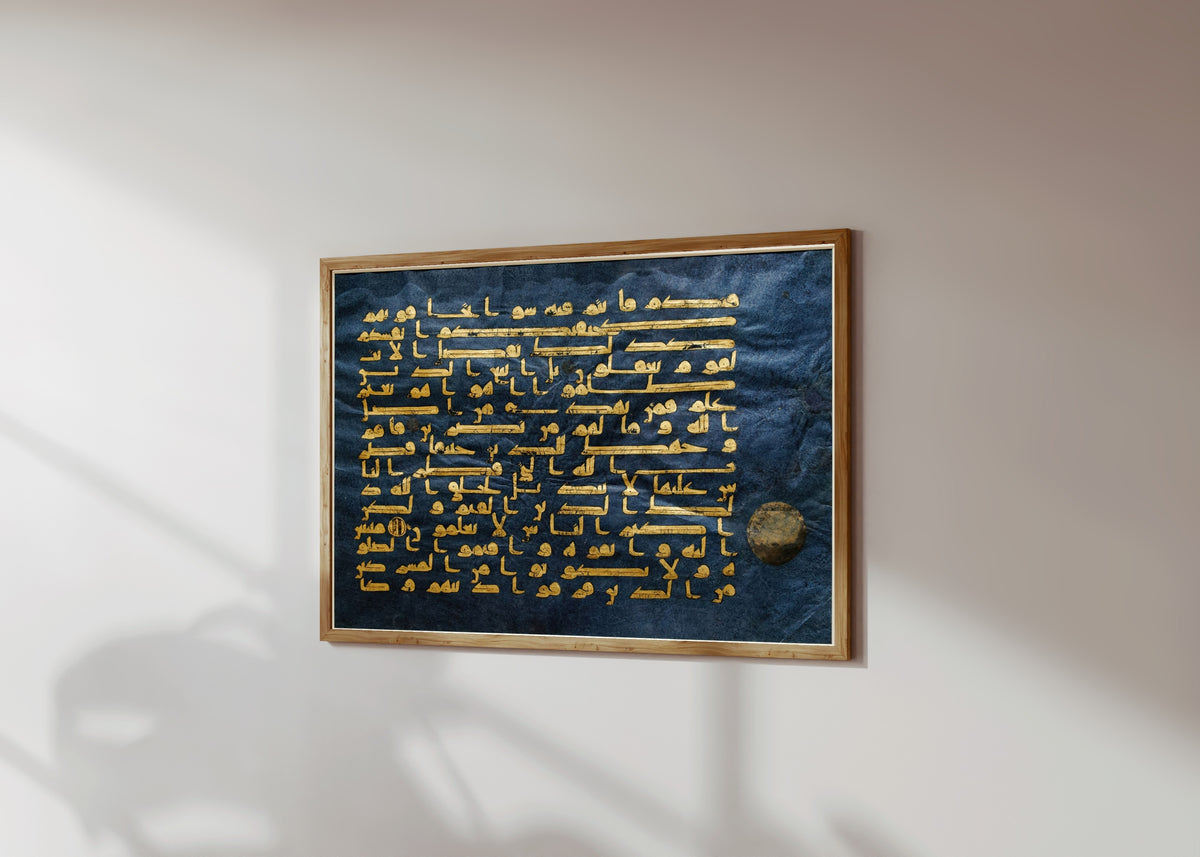 Framed art print of Ancient Islamic Calligraphy Art Print by The Blue Qur'an, in a light wood frame on a sunlit white wall, seen at a slight angle