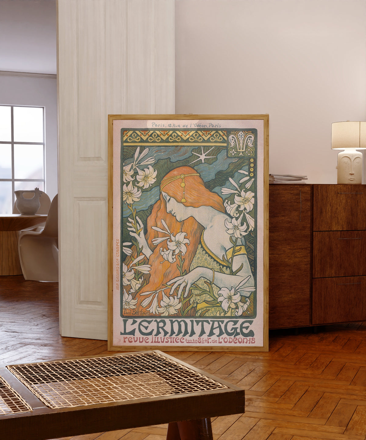 Framed art print of L'Ermitage by Paul Berthon, in a light wood frame leaning in a warm room with a parquet floor