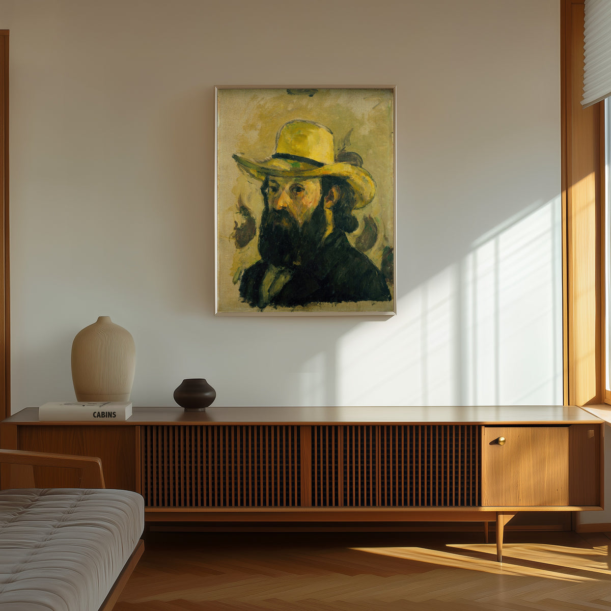 Framed art print of Self-Portrait in a Straw Hat by Paul Cezanne, in a thin light frame on a sunlit wall above a wooden sideboard