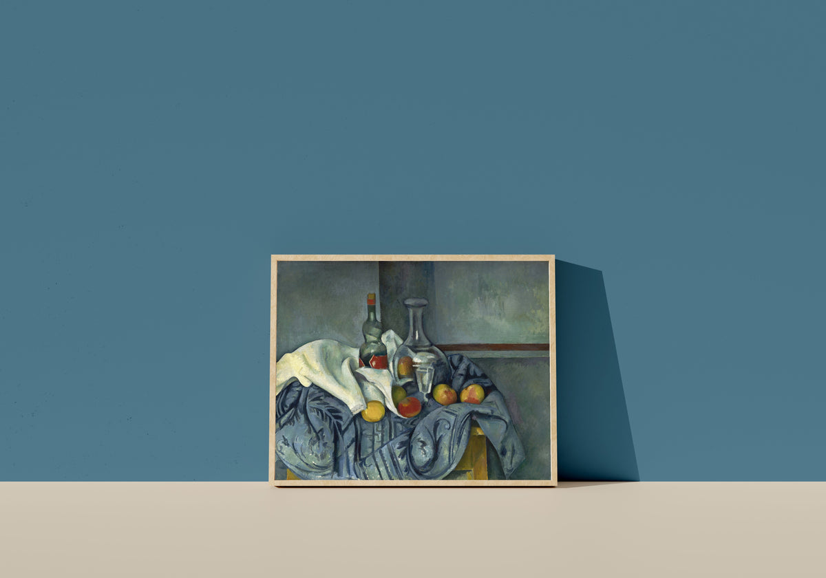 Framed art print of The Peppermint Bottle by Paul Cezanne, in a light wood frame leaning on a blue wall