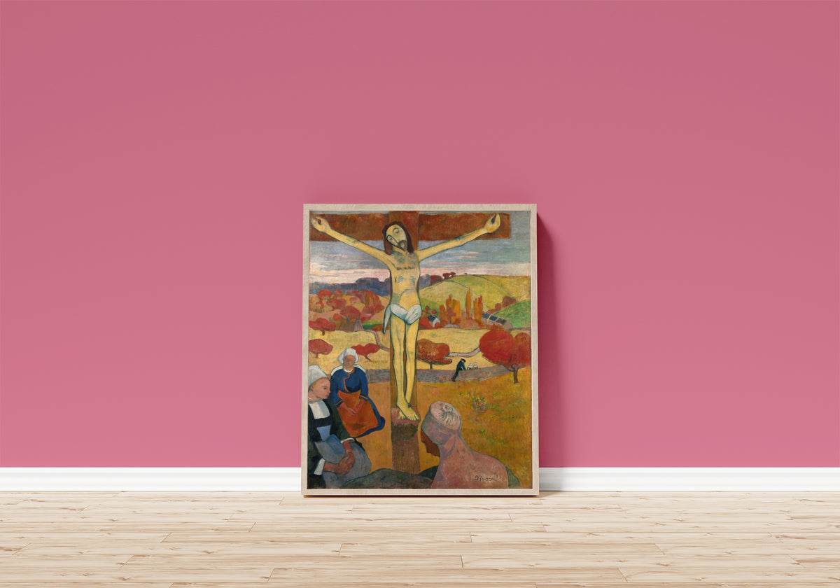 Framed art print of The Yellow Christ by Paul Gauguin, in a light wood frame leaning on a pink wall above a wooden floor