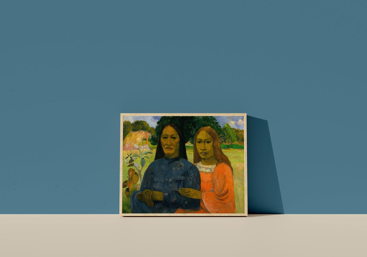 Framed art print of Two Women by Paul Gauguin, in a light wood frame leaning on a blue wall