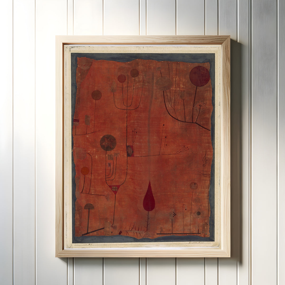 Framed art print of Fruits on Red (Früchte auf Rot) by Paul Klee, in a light wood frame on a white panelled wall