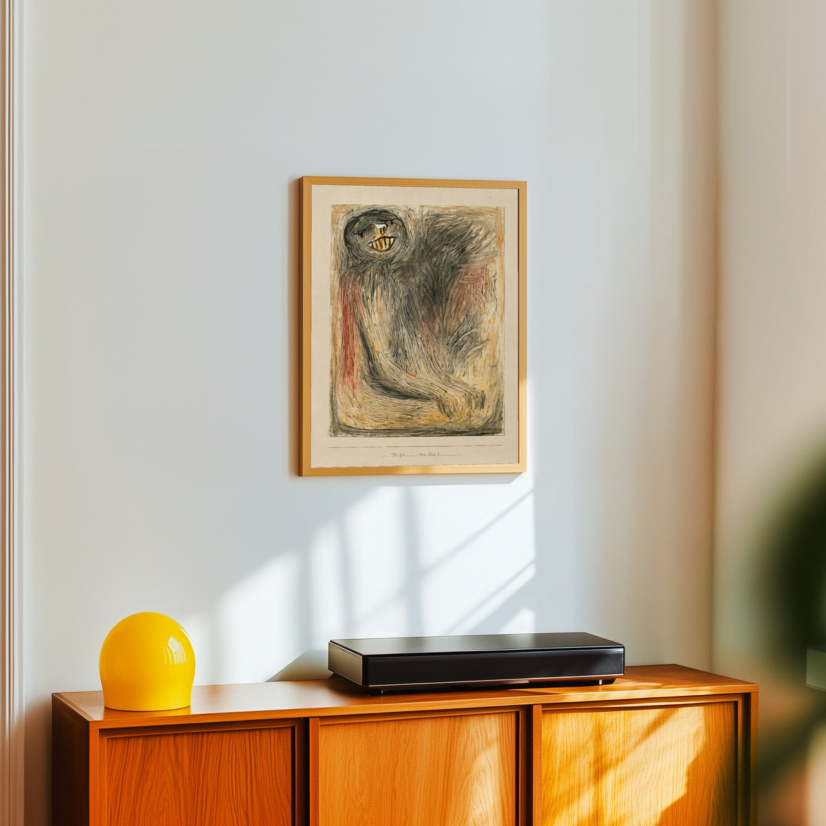 Framed art print of Your Ancestor (Dein Ahn) by Paul Klee, in a light wood frame on a white wall above an orange sideboard