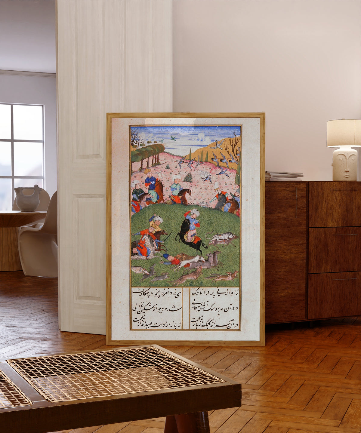 Framed art print of Khusrau and Shirin: Khusrau Hunting with His Companions by Suzi, in a light wood frame leaning in a warm room with a parquet floor