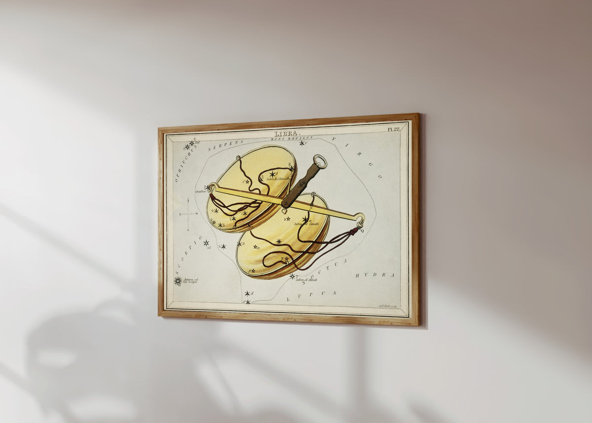 Framed art print of Libra by Sidney Hall, in a light wood frame on a sunlit white wall, seen at a slight angle