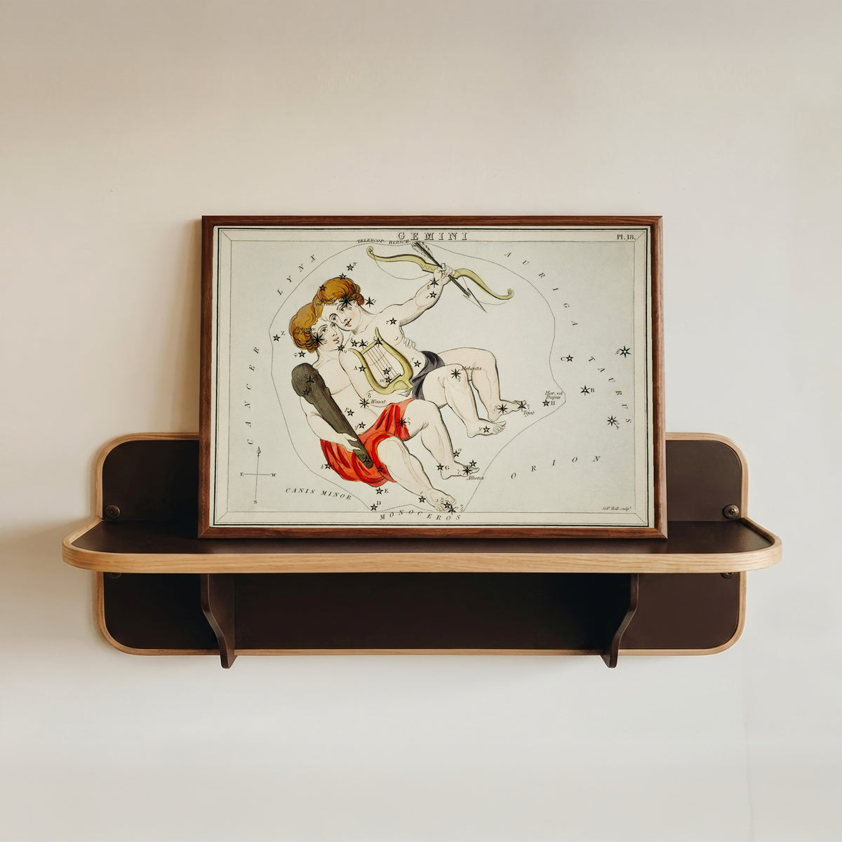 Framed art print of Gemini by Sidney Hall, in a dark wood frame resting on a wall shelf