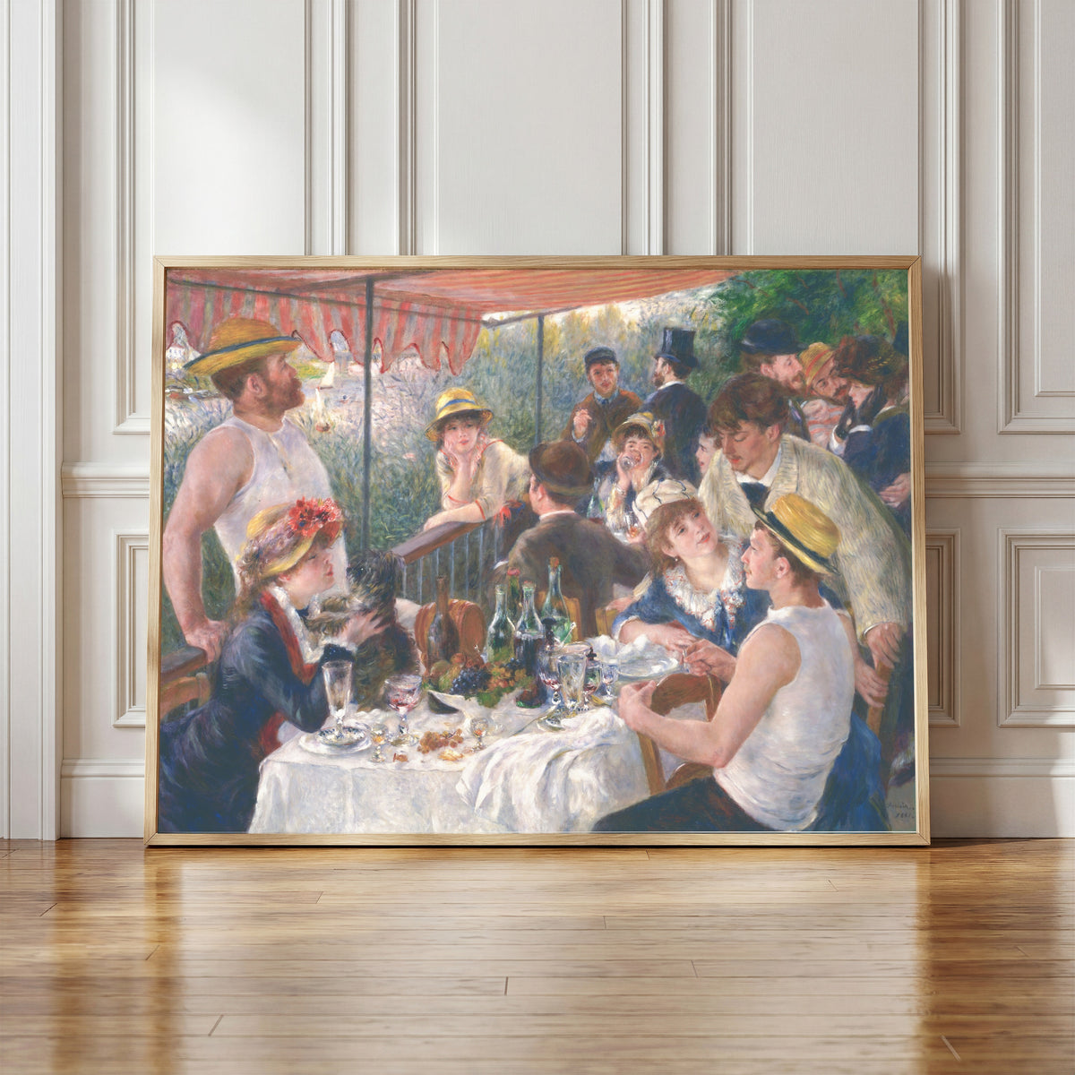 Framed art print of Luncheon of the Boating Party by Pierre-Auguste Renoir, in a light wood frame leaning against a panelled white wall