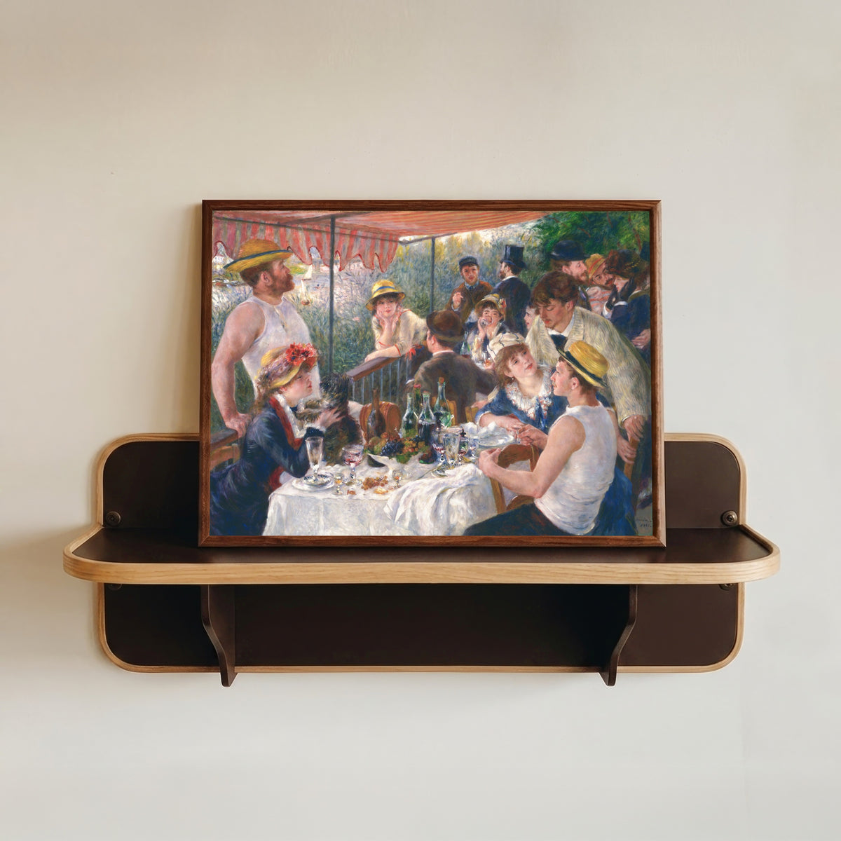 Framed art print of Luncheon of the Boating Party by Pierre-Auguste Renoir, in a dark wood frame resting on a wall shelf