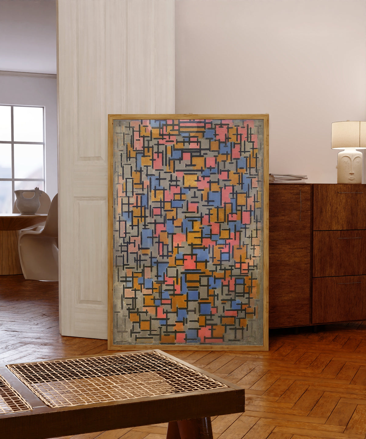 Framed art print of Composition by Piet Mondrian, in a light wood frame leaning in a warm room with a parquet floor