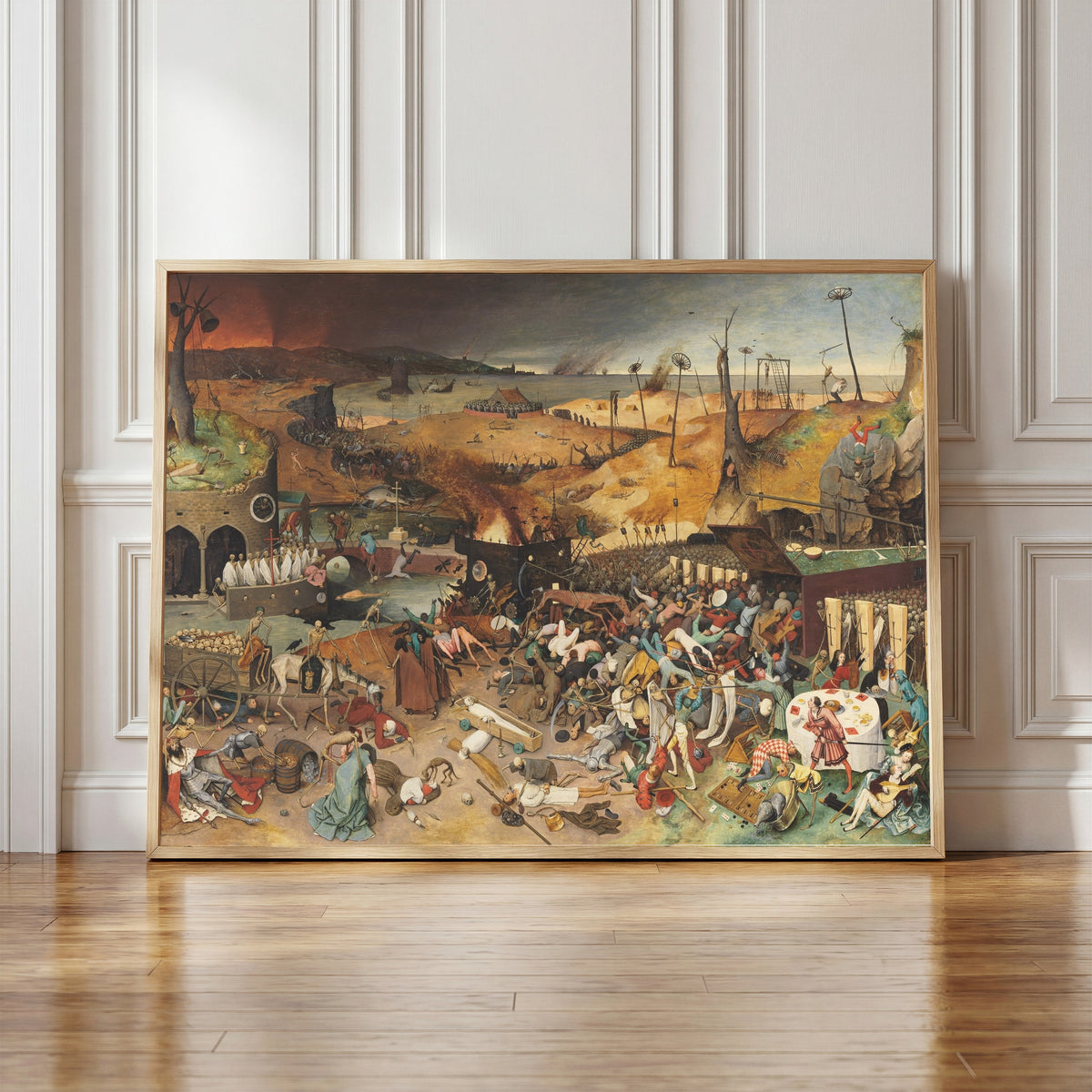 Framed art print of The Triumph of Death by Pieter Bruegel the Elder, in a light wood frame leaning against a panelled white wall