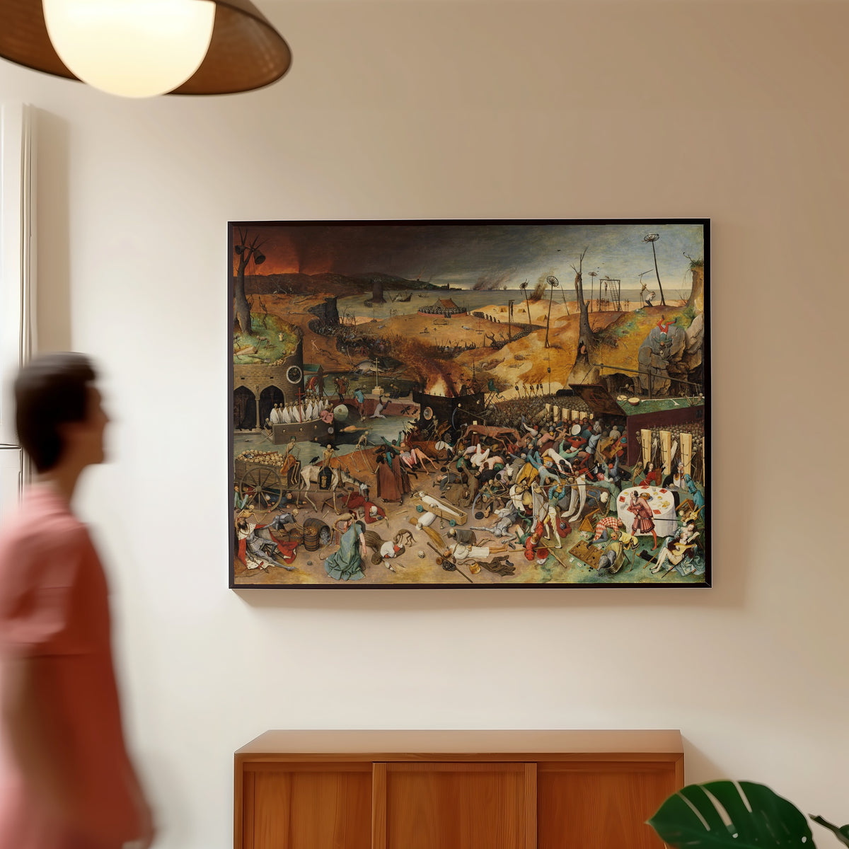 Framed art print of The Triumph of Death by Pieter Bruegel the Elder, in a slim black frame on a warm wall in a sunlit room