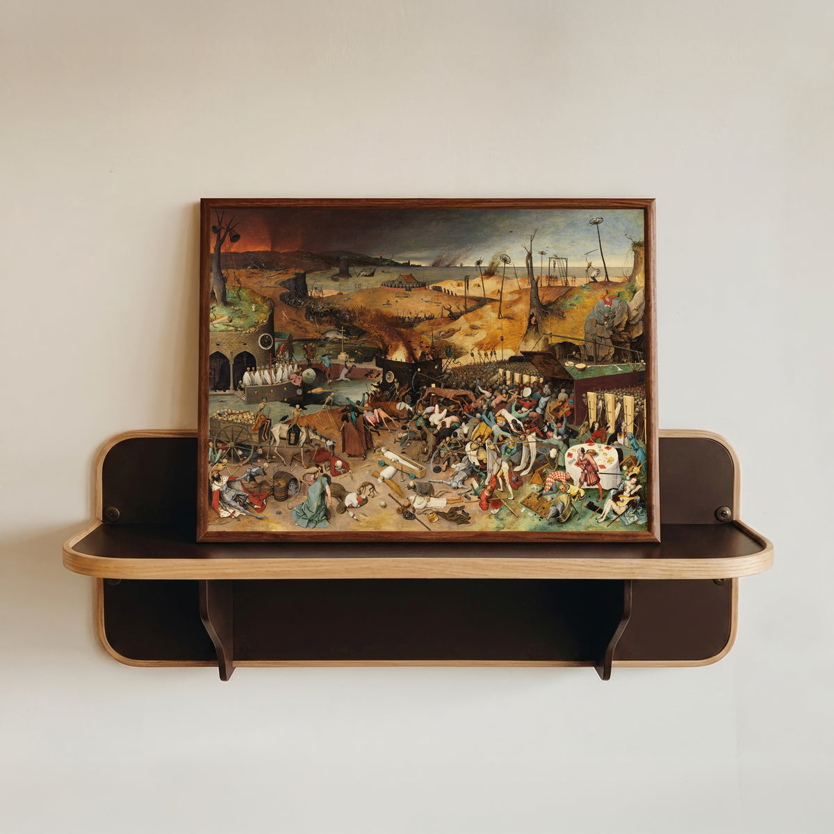 Framed art print of The Triumph of Death by Pieter Bruegel the Elder, in a dark wood frame resting on a wall shelf
