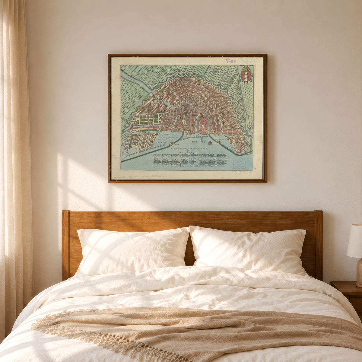 Framed art print of Plan de la Ville d'Amsterdam, in a slim wood frame above a bed in a sunlit bedroom