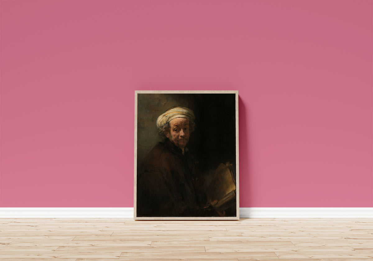 Framed art print of Self-portrait as the Apostle Paul by Rembrandt van Rijn, in a light wood frame leaning on a pink wall above a wooden floor