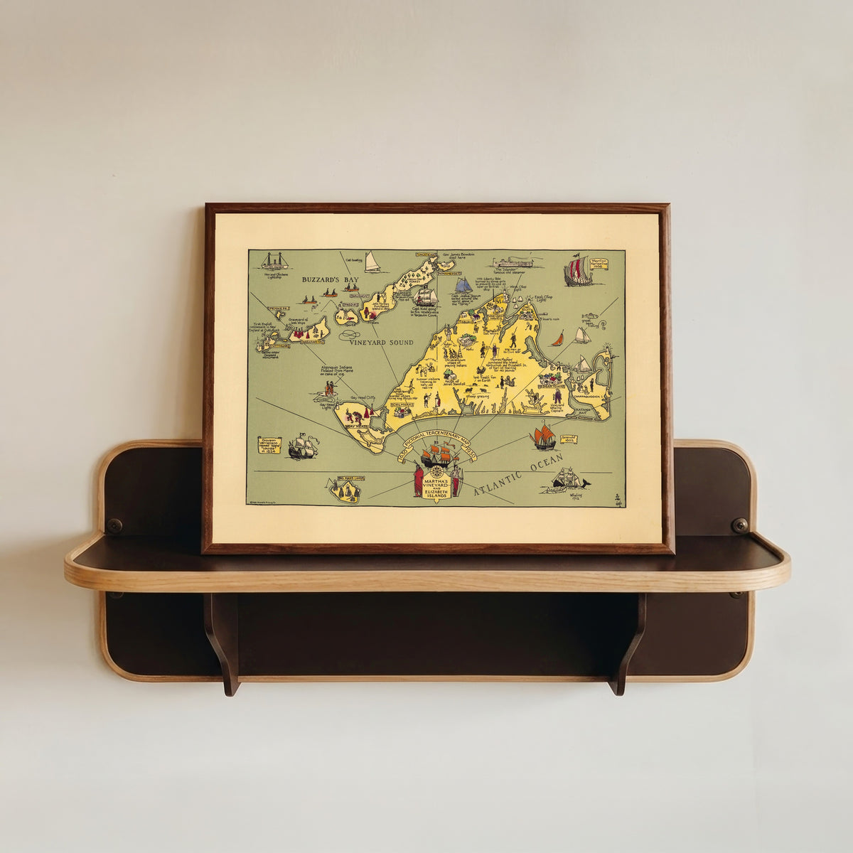 Framed art print of Pictorial Tercentenary Map of Martha's Vineyard and Elizabeth… by Reynold's Printing Co., in a dark wood frame resting on a wall shelf