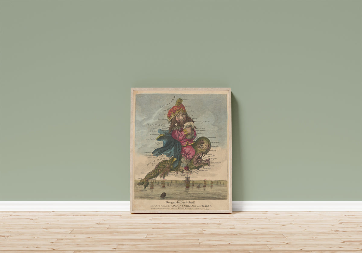 Framed art print of Geography Bewitched! A Droll Caricature Map of… by Robert Dighton, in a light wood frame leaning on a sage green wall above a wooden floor