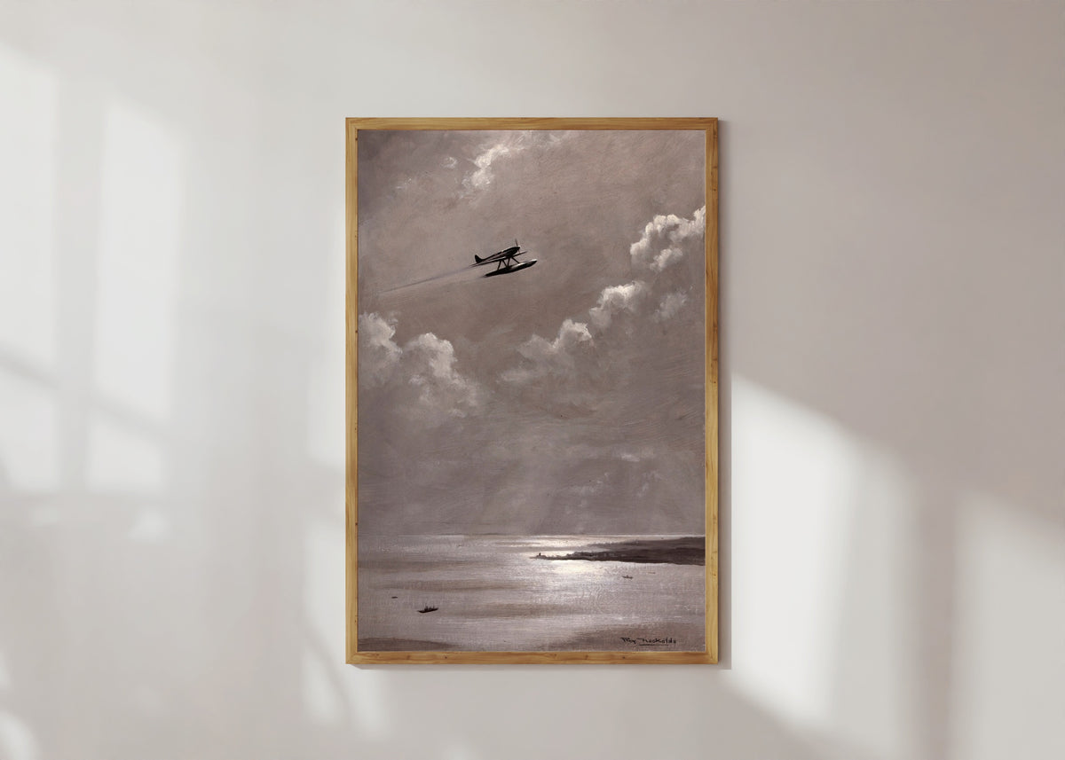 Framed art print of Seaplane over the Coast by Roy Nockolds, in a light wood frame on a sunlit white wall