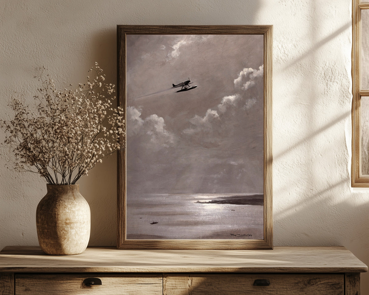 Framed art print of Seaplane over the Coast by Roy Nockolds, in a dark wood frame leaning on a rustic console beside dried flowers