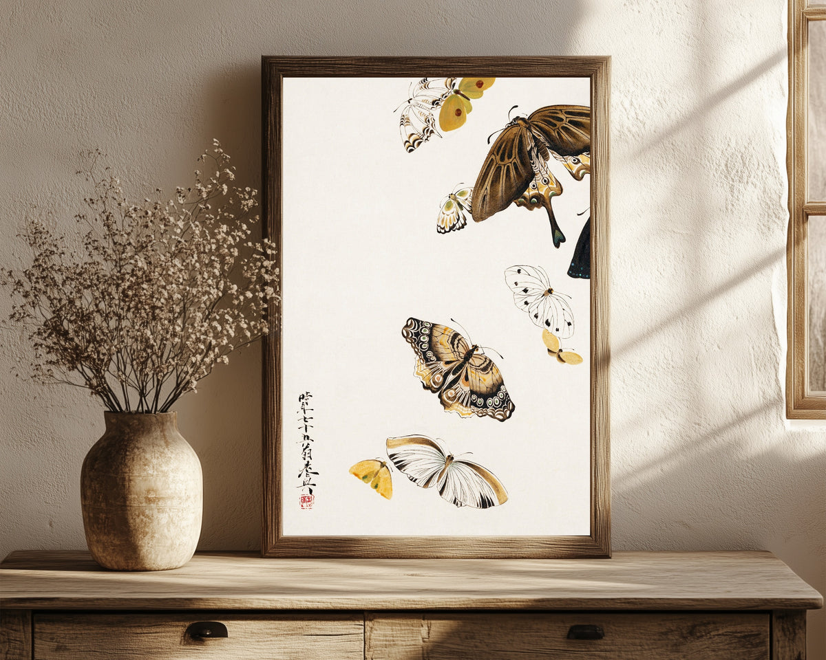 Framed art print of Butterflies by Shibata Zeshin, in a dark wood frame leaning on a rustic console beside dried flowers
