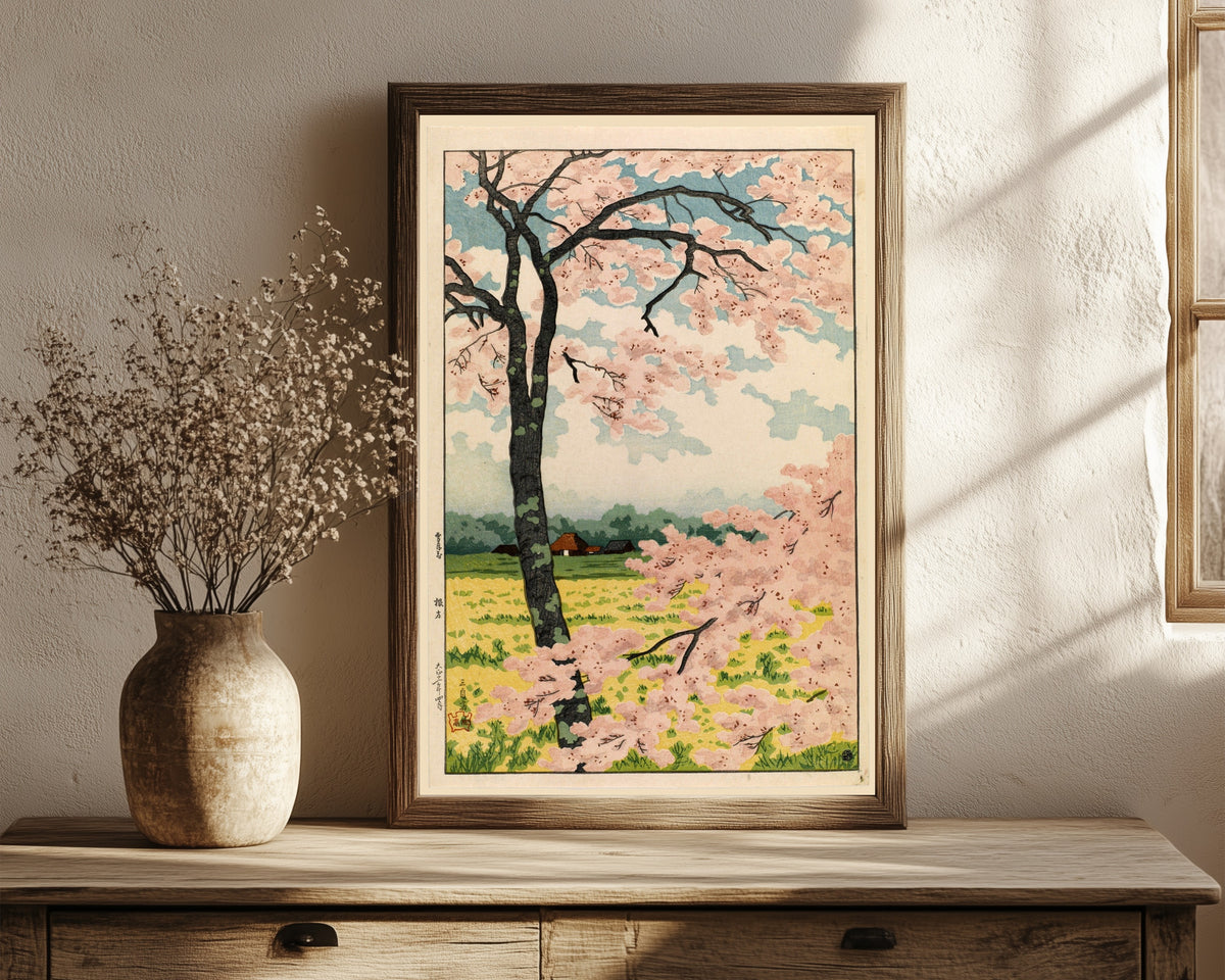 Framed art print of Nekata (Cherry Blossoms) by Takahashi Shotei, in a dark wood frame leaning on a rustic console beside dried flowers