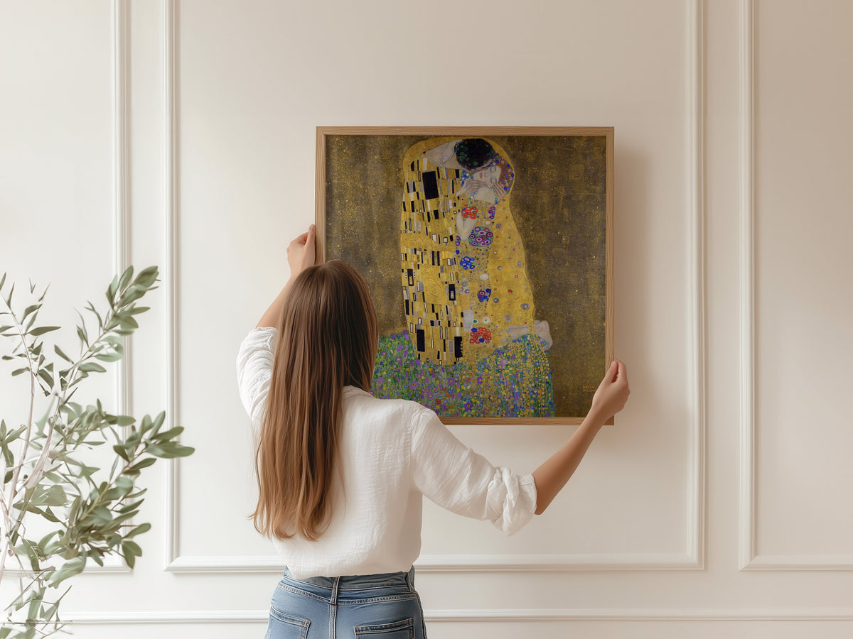 A woman hanging a framed print of Gustav Klimt — The Kiss