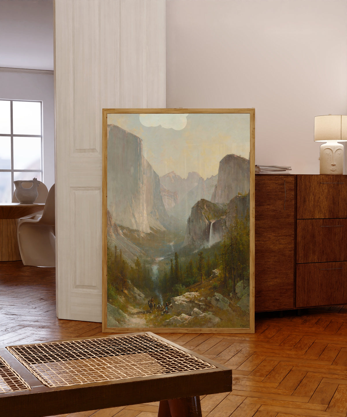 Framed art print of Yosemite Valley by Thomas Hill, in a light wood frame leaning in a warm room with a parquet floor