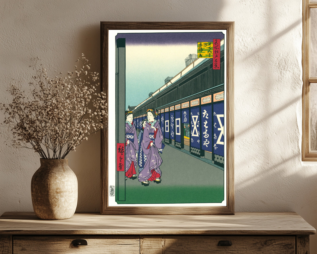Framed art print of Shops with Cotton Goods in Ōdenma-chō by Utagawa Hiroshige, in a dark wood frame leaning on a rustic console beside dried flowers