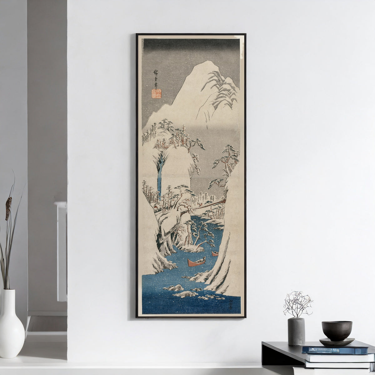 The Fuji River in the Snow by Utagawa Hiroshige — framed on a white wall above books and a bowl