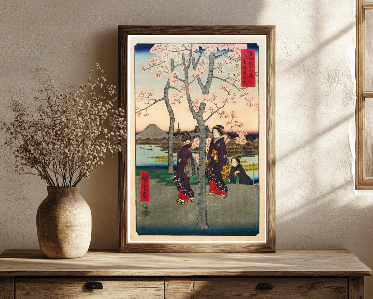 Framed art print of The Sumida Embankment in the Eastern Capital by Utagawa Hiroshige, in a dark wood frame leaning on a rustic console beside dried flowers