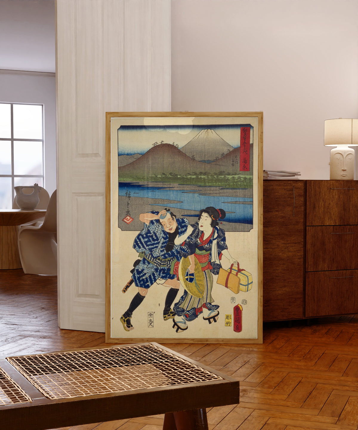 Framed art print of Fifty-three Stations by Two… by Utagawa Hiroshige & Utagawa Kunisada, in a light wood frame leaning in a warm room with a parquet floor