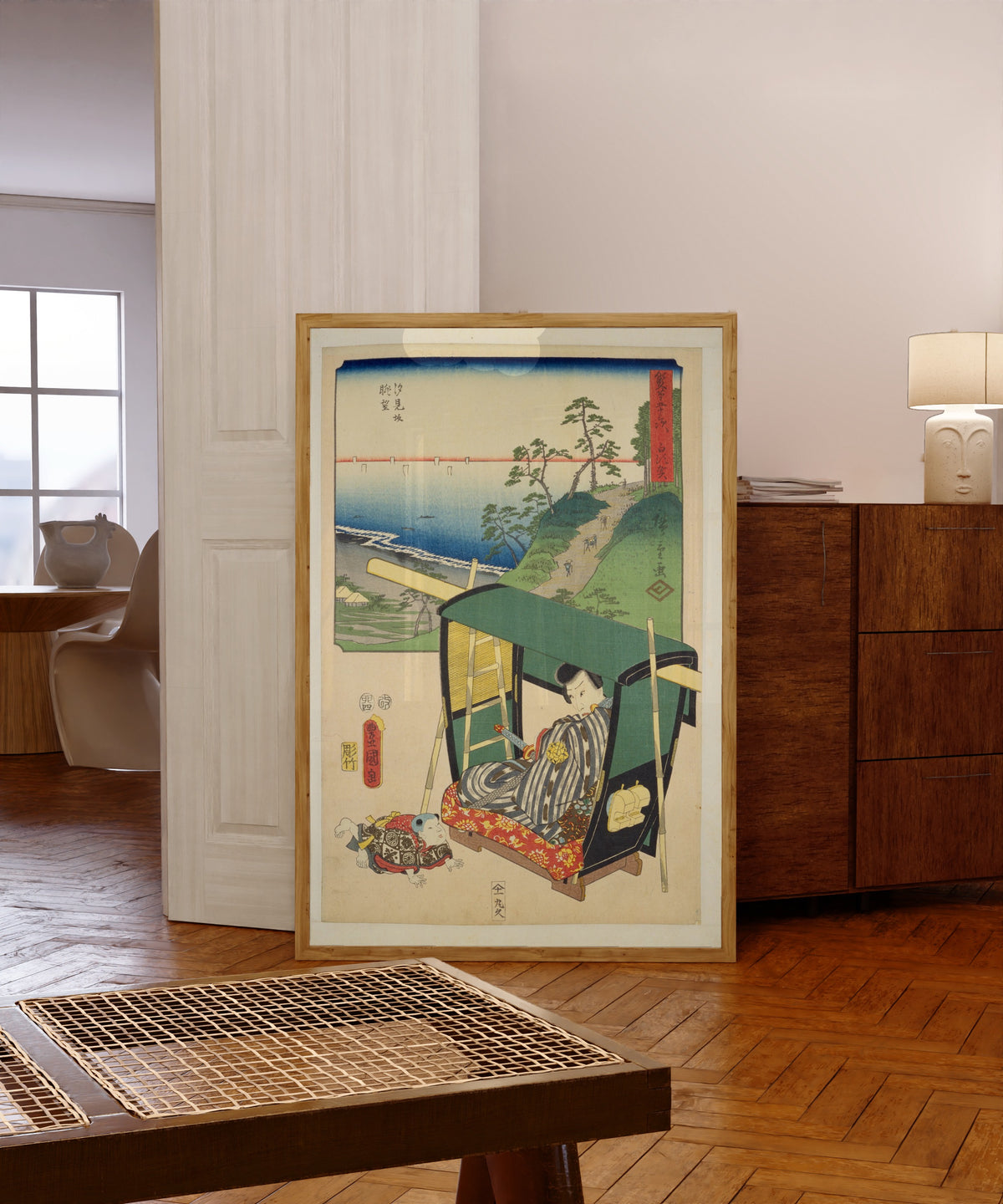 Framed art print of Fifty-three Stations by Two… by Utagawa Hiroshige & Utagawa Kunisada, in a light wood frame leaning in a warm room with a parquet floor