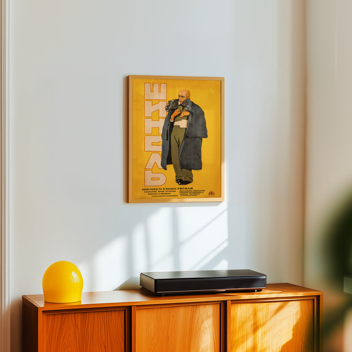 Framed art print of The Overcoat (Gogol) by Alexander Zelensky, in a light wood frame on a white wall above an orange sideboard