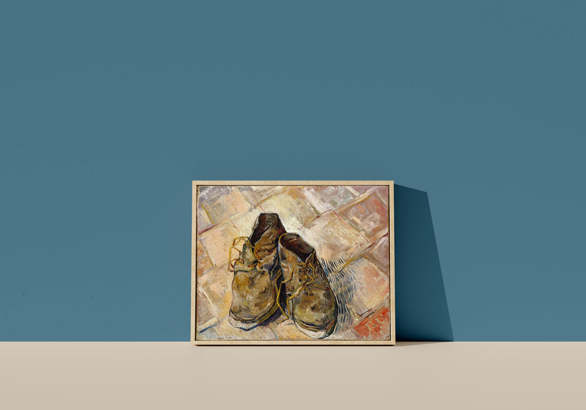 Framed art print of Shoes by Vincent van Gogh, in a light wood frame leaning on a blue wall