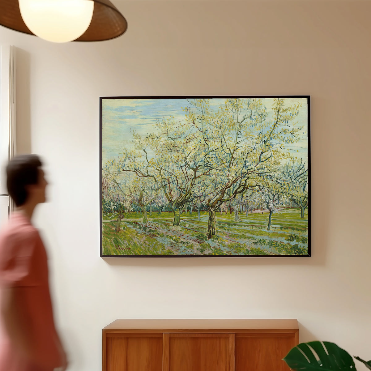 Framed art print of The White Orchard by Vincent van Gogh, in a slim black frame on a warm wall in a sunlit room