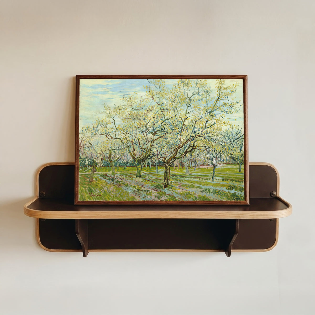 Framed art print of The White Orchard by Vincent van Gogh, in a dark wood frame resting on a wall shelf