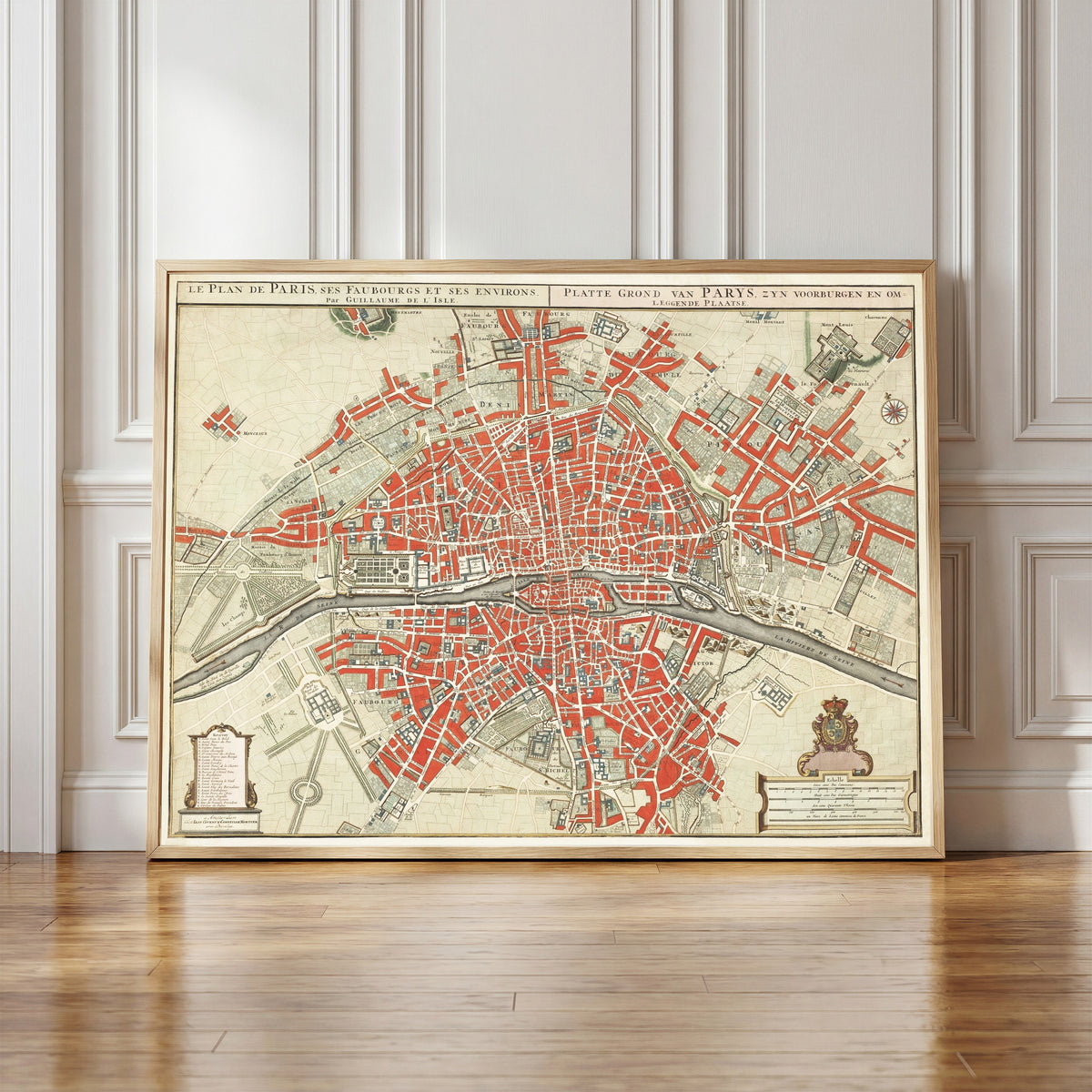 Framed art print of Le Plan de Paris, ses Faubourgs et ses Environs by Guillaume de l'Isle, in a light wood frame leaning against a panelled white wall