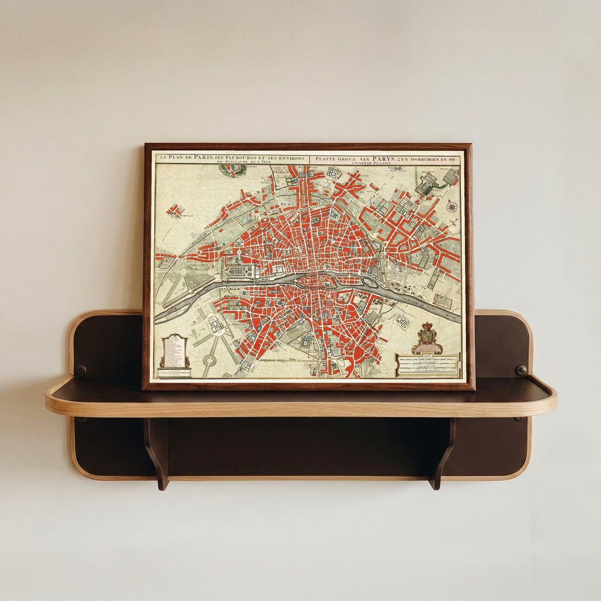 Framed art print of Le Plan de Paris, ses Faubourgs et ses Environs by Guillaume de l'Isle, in a dark wood frame resting on a wall shelf