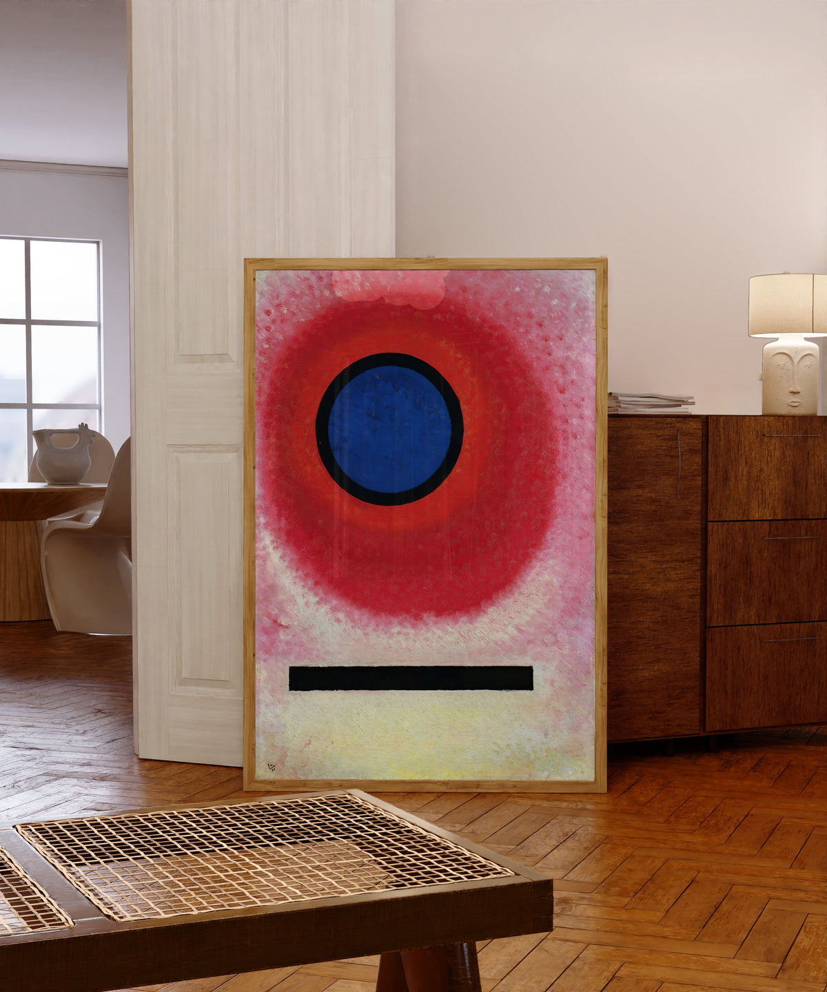 Framed art print of Blue Circle 2 by Wassily Kandinsky, in a light wood frame leaning in a warm room with a parquet floor