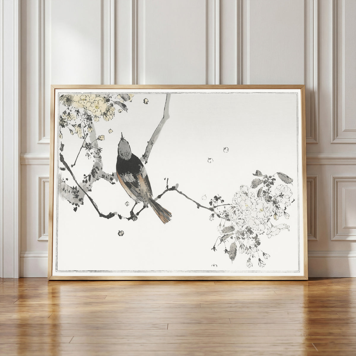 Framed art print of Bird on a Flowering Branch by Watanabe Seitei, in a light wood frame leaning against a panelled white wall