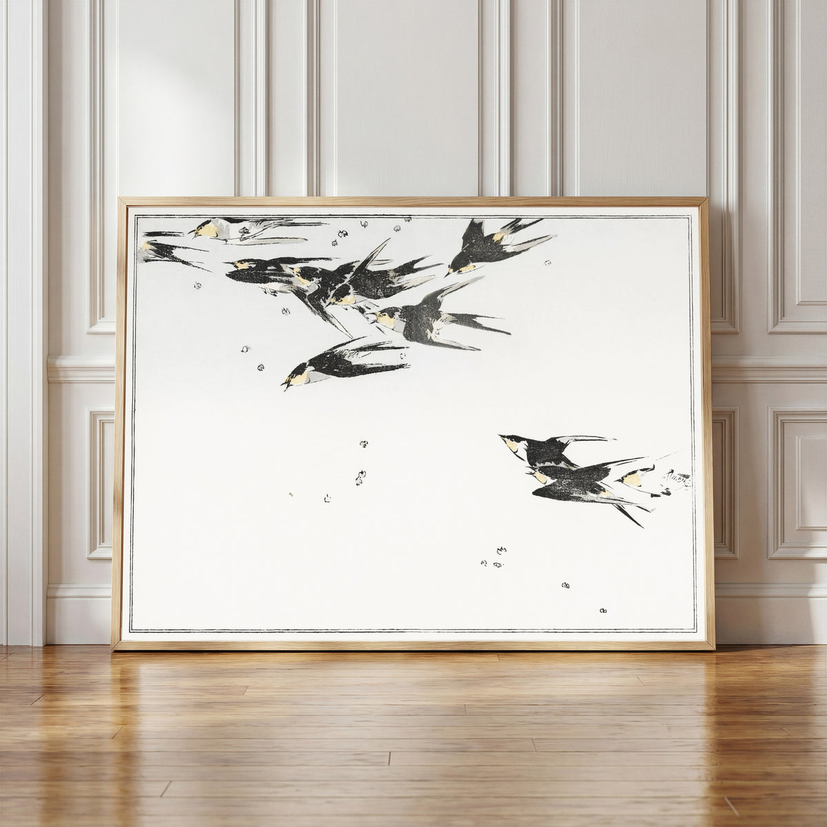 Framed art print of Swallows in Flight by Watanabe Seitei, in a light wood frame leaning against a panelled white wall