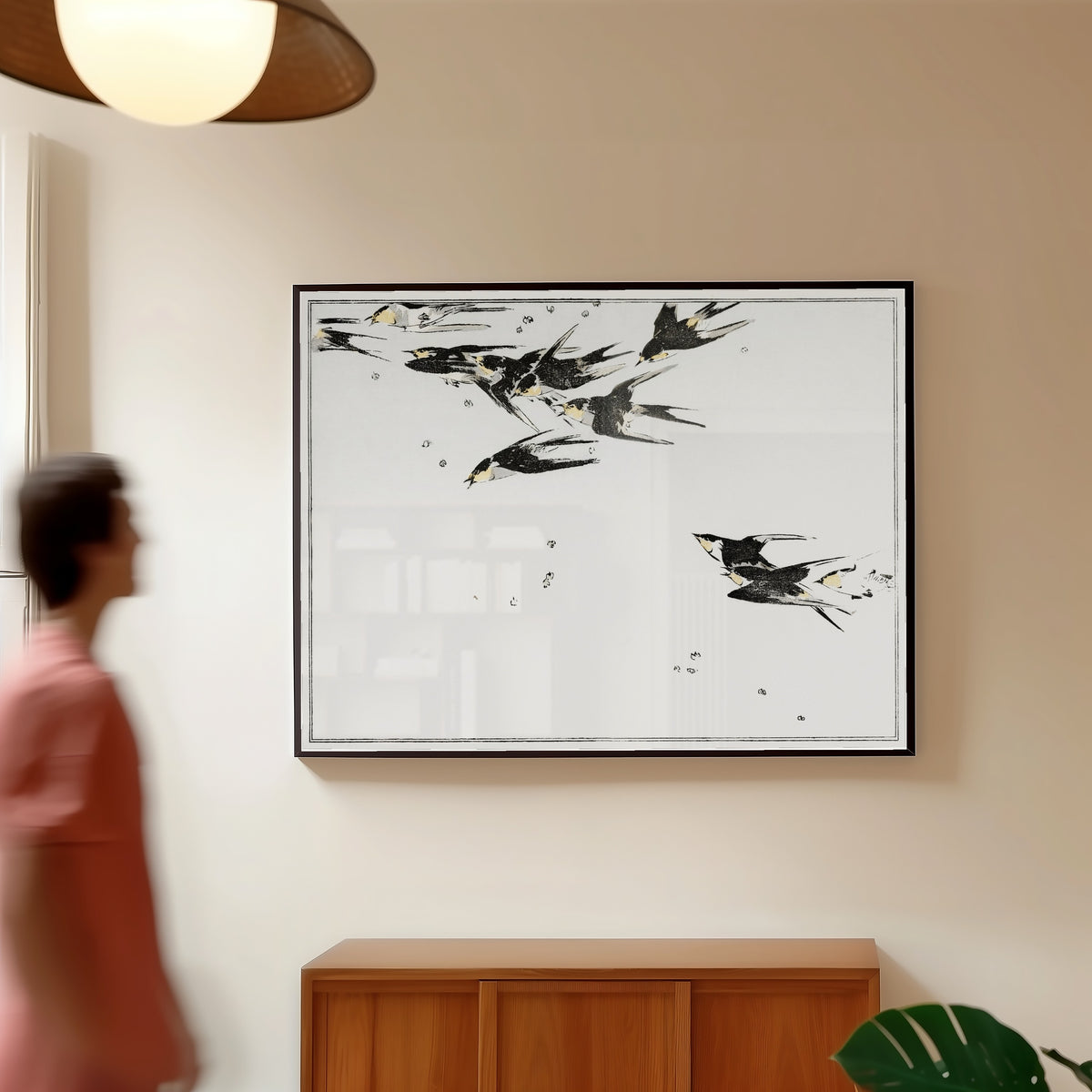Framed art print of Swallows in Flight by Watanabe Seitei, in a slim black frame on a warm wall in a sunlit room