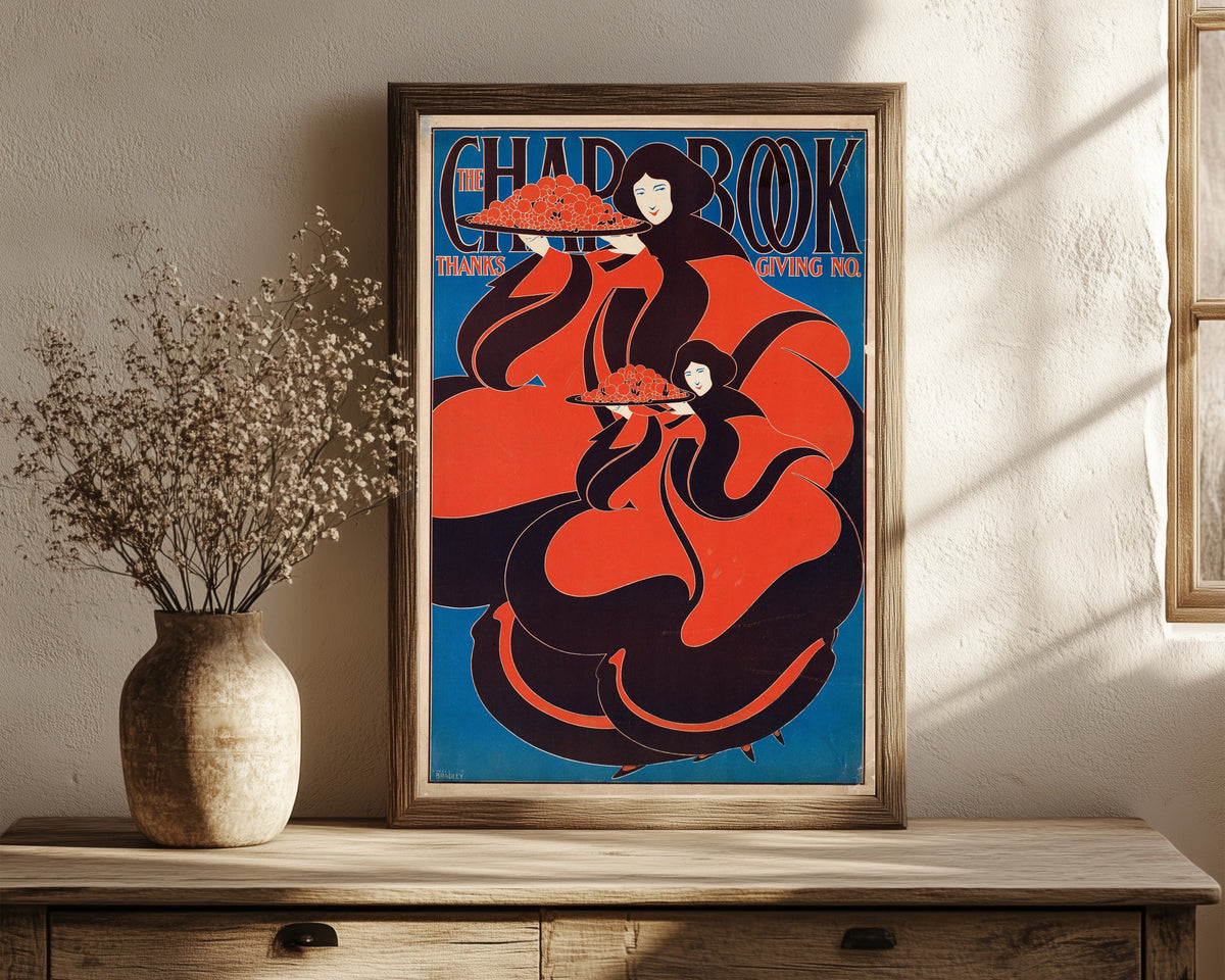 Framed art print of The Chap-Book, Thanksgiving Number, 1895 by Will Bradley, in a dark wood frame leaning on a rustic console beside dried flowers